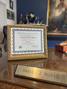 A framed "CERTIFICATE OF RECOGNITION" for "Daniel Jason Russo" sits on a desk next to a "DANIEL J. RUSSO" nameplate. This professional display highlights a significant career achievement.
